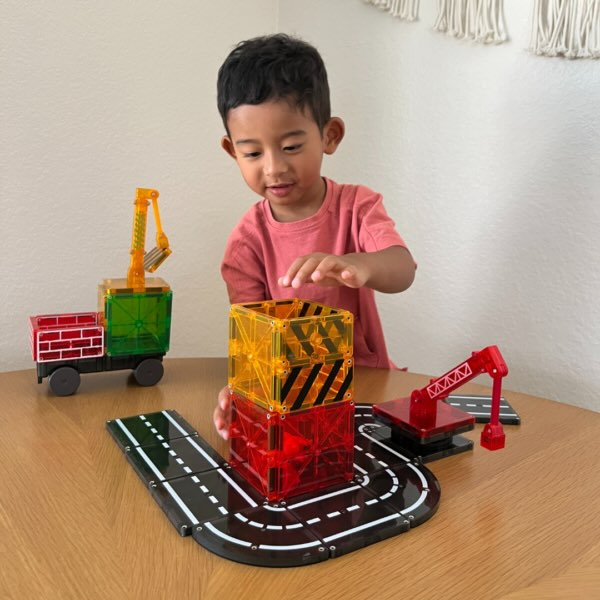 Jongen speelt thuis met Magnetic Magna Tiles Builder set, wegdelen en kraan, met magnetische bouwstenen magneet speelgoed.