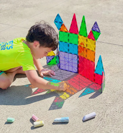 Jonge jongen tekent met krijt naast kasteel van Magnetic Magna Tiles Classic Set, 32 magnetische bouwstenen speelgoed.