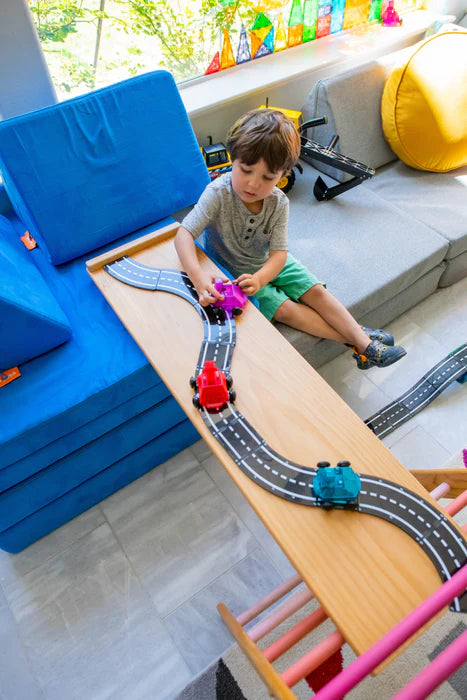 Kind speelt met de Magnetic Magna Tiles Downhill Duo, met een blauw en rood voertuig op een schuine racebaan in de woonkamer.