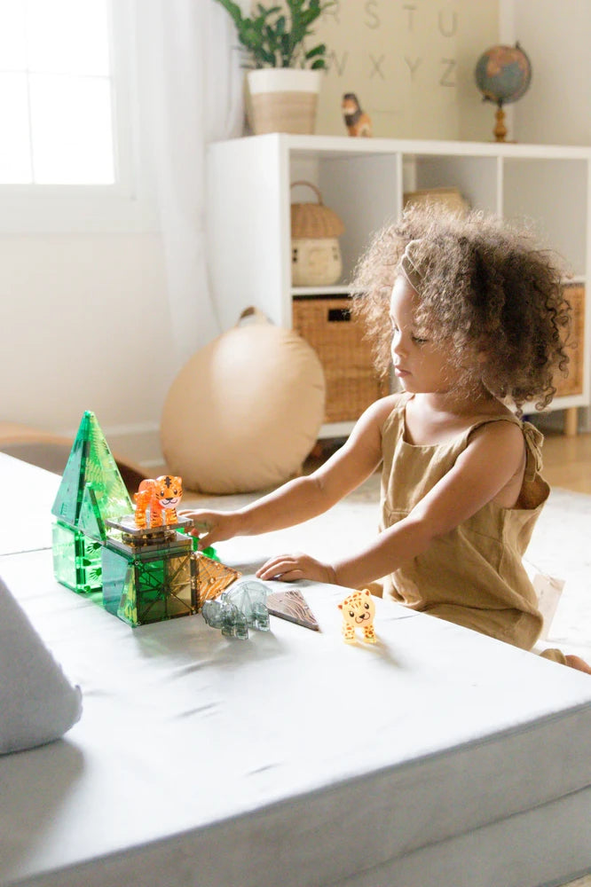 Kind speelt met magnetisch speelgoed van Magna Tiles Jungle Animals met tijger en leeuw in lichte speelhoek met houten meubels.