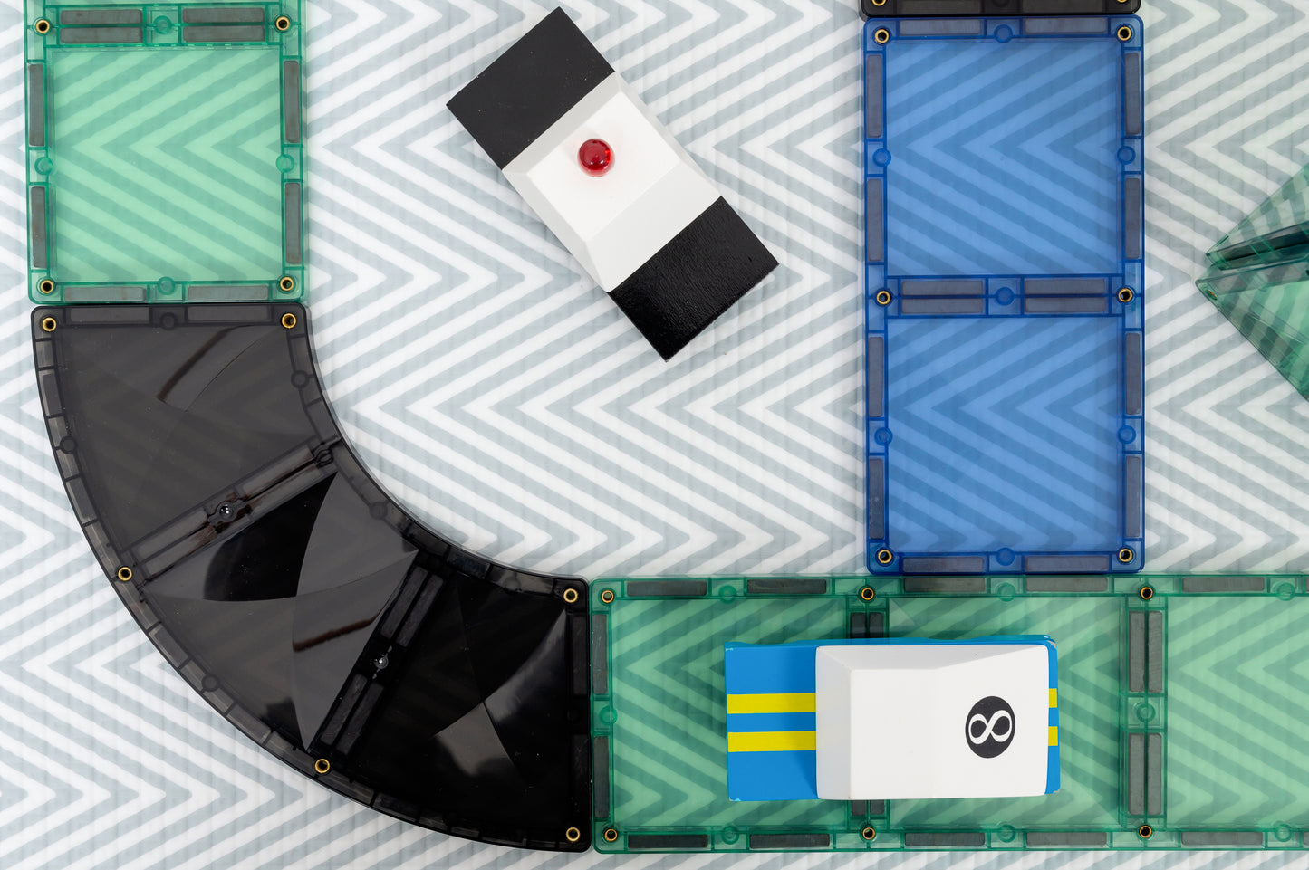 Magnetisch speelgoed Connetix detail close-up met zwarte bocht, gekleurde tegels en speelgoedauto bovenaanzicht