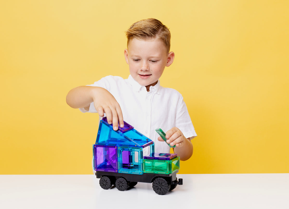 Kind bouwt vrachtwagen met Connetix Transport Bright Pack 50 magnetisch speelgoed op gele achtergrond