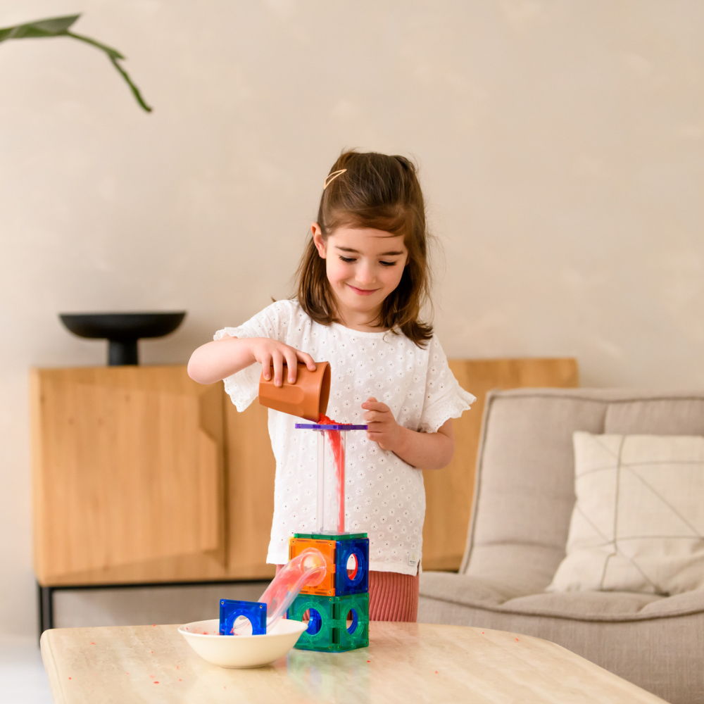 Meisje speelt met Coblo knikkerbaan magnetische tegels en bouwt kleurrijke constructie met knikkers