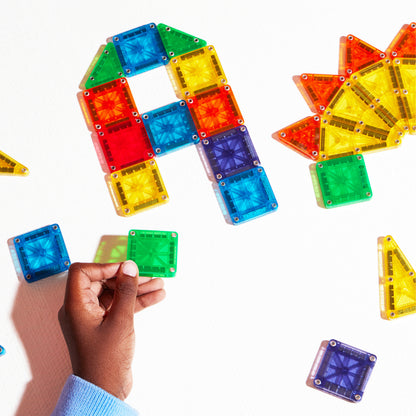 Bovenaanzicht magnetic magna tiles met hand die groene magnetische tegel vasthoudt en kleurrijke bouwvormen