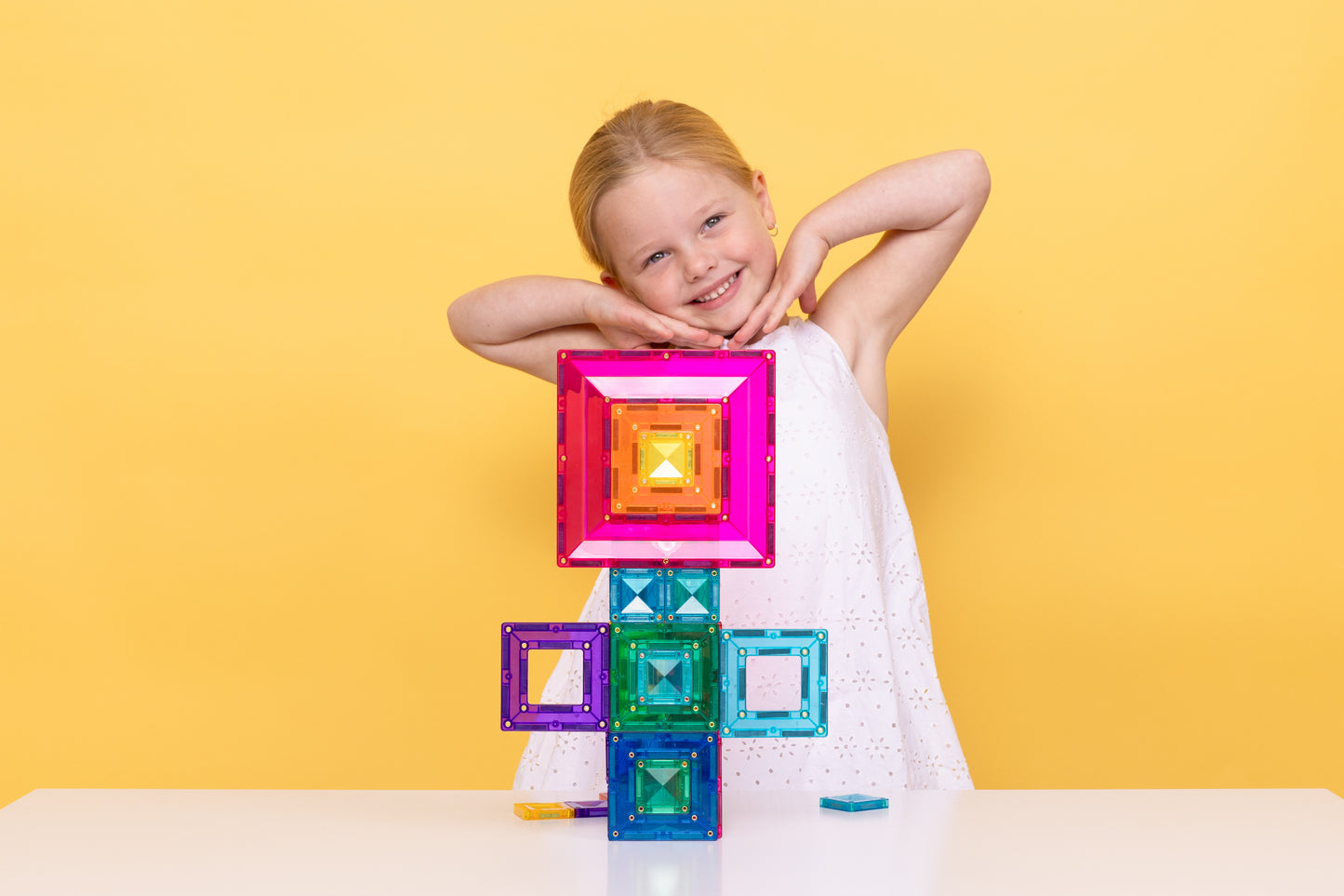 Meisje leunt op gestapelde Connetix Bright Portal Pack 48pc magnetische tegels, gele achtergrond