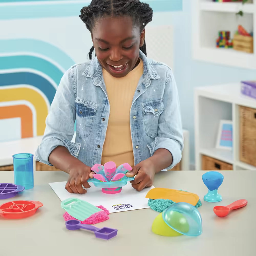 Meisje maakt bloemvorm uit roze en blauw Kinetic Sand met turquoise mal; sensorisch speelgoed prikkelt fijne motoriek.