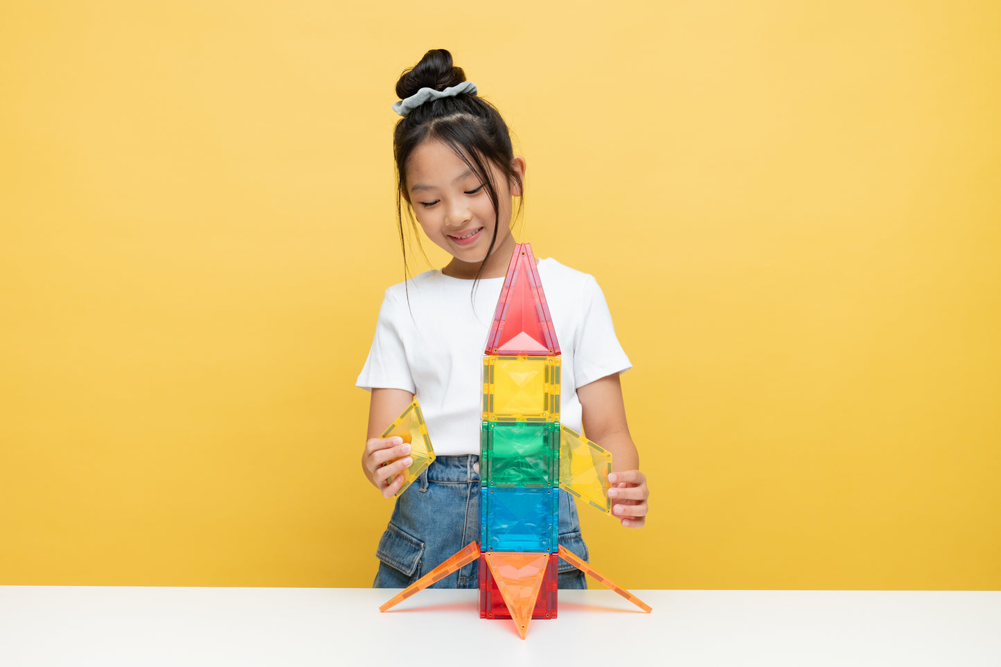 Magnetische tegels Connetix raket gebouwd door spelend meisje, gele achtergrond, creatief spel