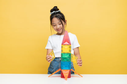 Magnetische tegels Connetix raket gebouwd door spelend meisje, gele achtergrond, creatief spel