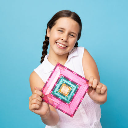 Meisje toont Connetix Pastel magnetische tegels constructie op blauwe achtergrond met groot portaalframe