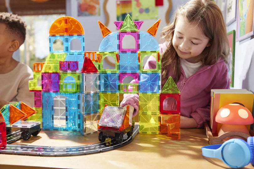 Meisje rijdt met auto door stad gebouwd met City Center Magna Tiles, fantasierijk magneet speelgoed.