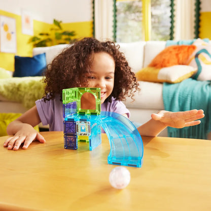 Kind rolt de Hamster Ball naar beneden over de blauwe glijbaan van de kleurrijke Magna Tiles speelset.