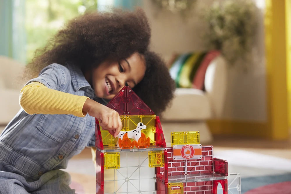 Meisje zet dalmatiër in magnetisch gebouw van Fire Station, gemaakt van kleurrijke magnetische tegels.