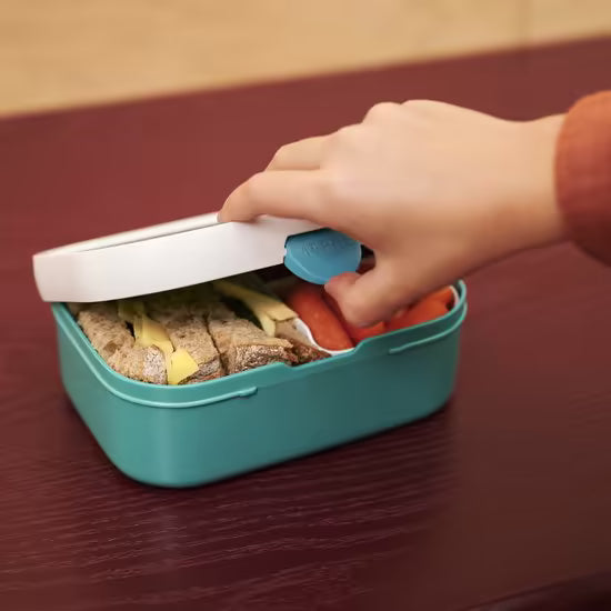 Kind opent groene Mepal lunchbox gevuld met brood en groente, ideaal voor gezonde en kindvriendelijke lunch