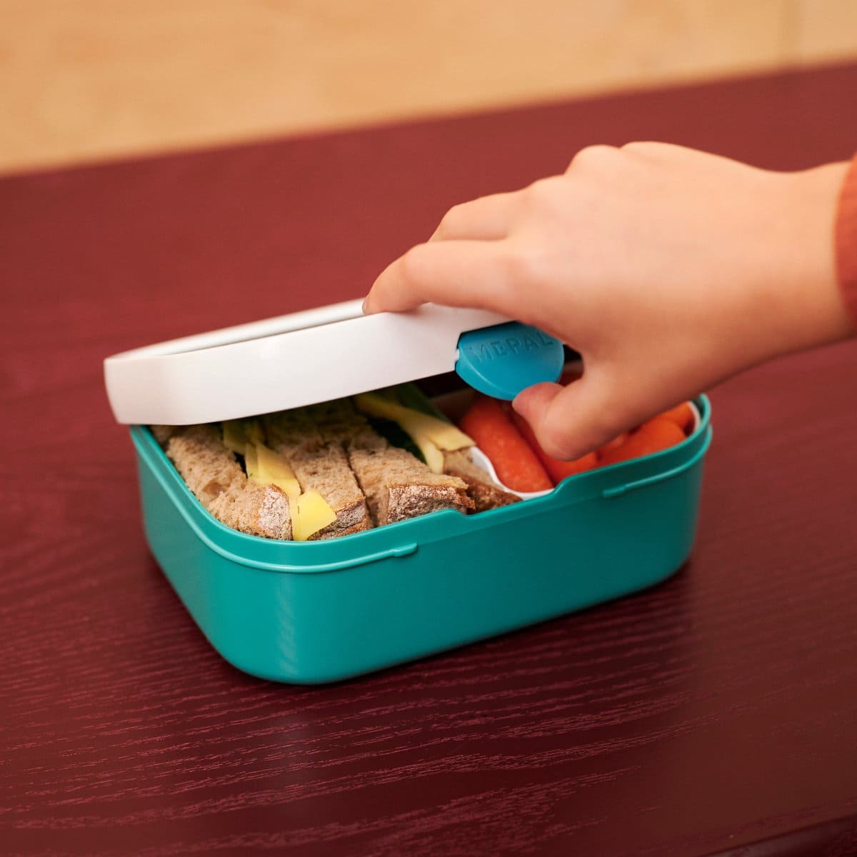 Kind opent groene Mepal lunchbox gevuld met brood en groente, ideaal voor gezonde en kindvriendelijke lunch