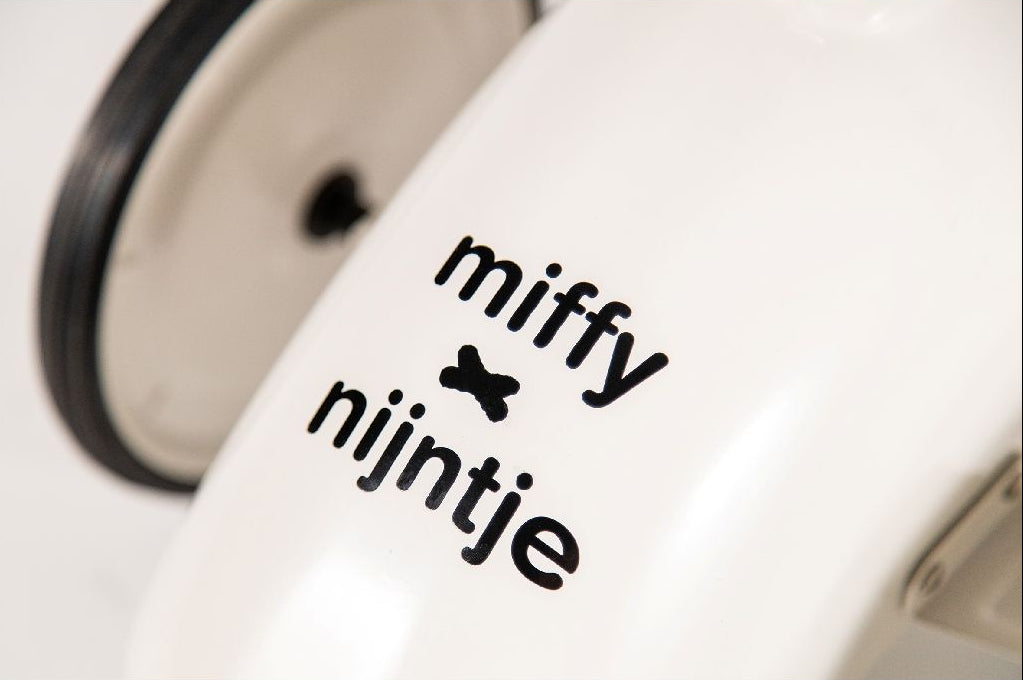 Detailfoto Miffy Nijntje logo op witte retro loopauto, zwarte letters met vlinder accent op carrosserie