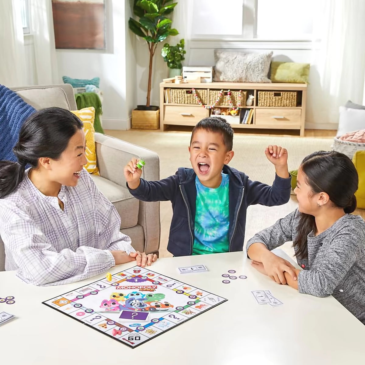 Kinderen spelen Monopoly Junior gezelschapsspel van Hasbro aan tafel, vrolijk familiespel voor thuis met jonge spelers.