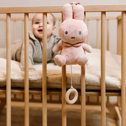 Muziekdoosje Nijntje in roze pluche met bloemmotief, baby speelt in ledikant met vrolijk muziekdoosje.