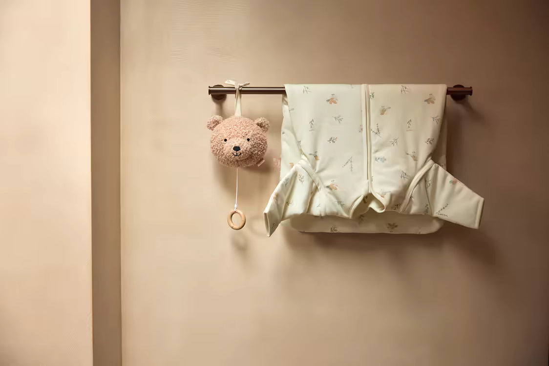 Jollein muziekdoosje Teddy bear in Wild Rose hangend naast babykleding op een kapstok, sfeervol baby cadeau.