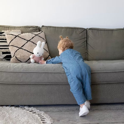 Kind speelt met Nijntje knuffel Fluffy Pink 25cm op groene bank, schattig kraamcadeau en sensorisch speelgoed.