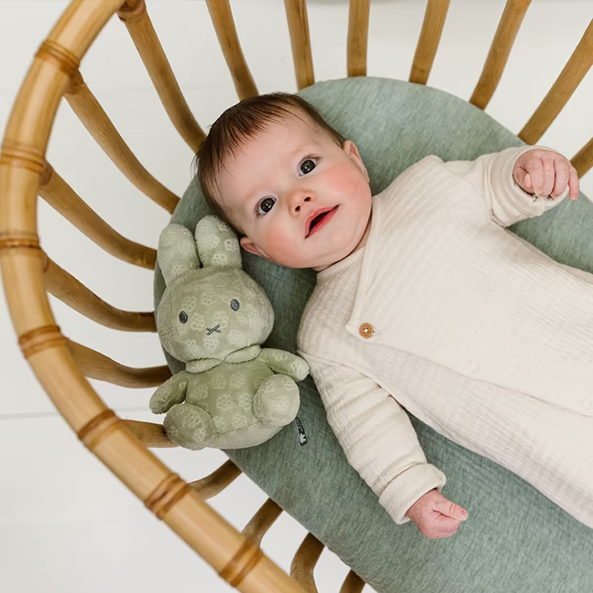 Baby in rotan wieg met zachte groene Nijntje knuffel Green Flower 20cm, perfect als liefdevol baby speelgoed.