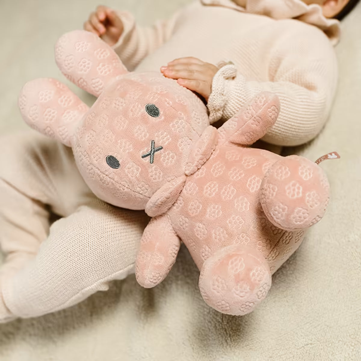 Liggende baby knuffelt roze Nijntje Knuffel 30cm, heerlijk zacht pluche en geschikt als sensorisch speelgoed.