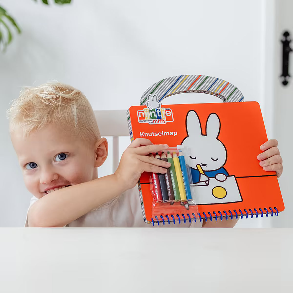 Kind toont Nijntje Knutselboek verpakking met vrolijke Miffy en kleurpotloden, ideaal voor knutselen met peuters.
