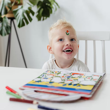 Blij kind speelt met Nijntje Knutselboek, sticker op voorhoofd en tekenboek op tafel voor met peuters knutselen.