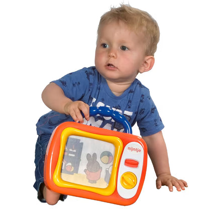 Baby kruipt en houdt Nijntje mijn eerste TV vast, vrolijk educatief speelgoed met kleurrijke figuren.