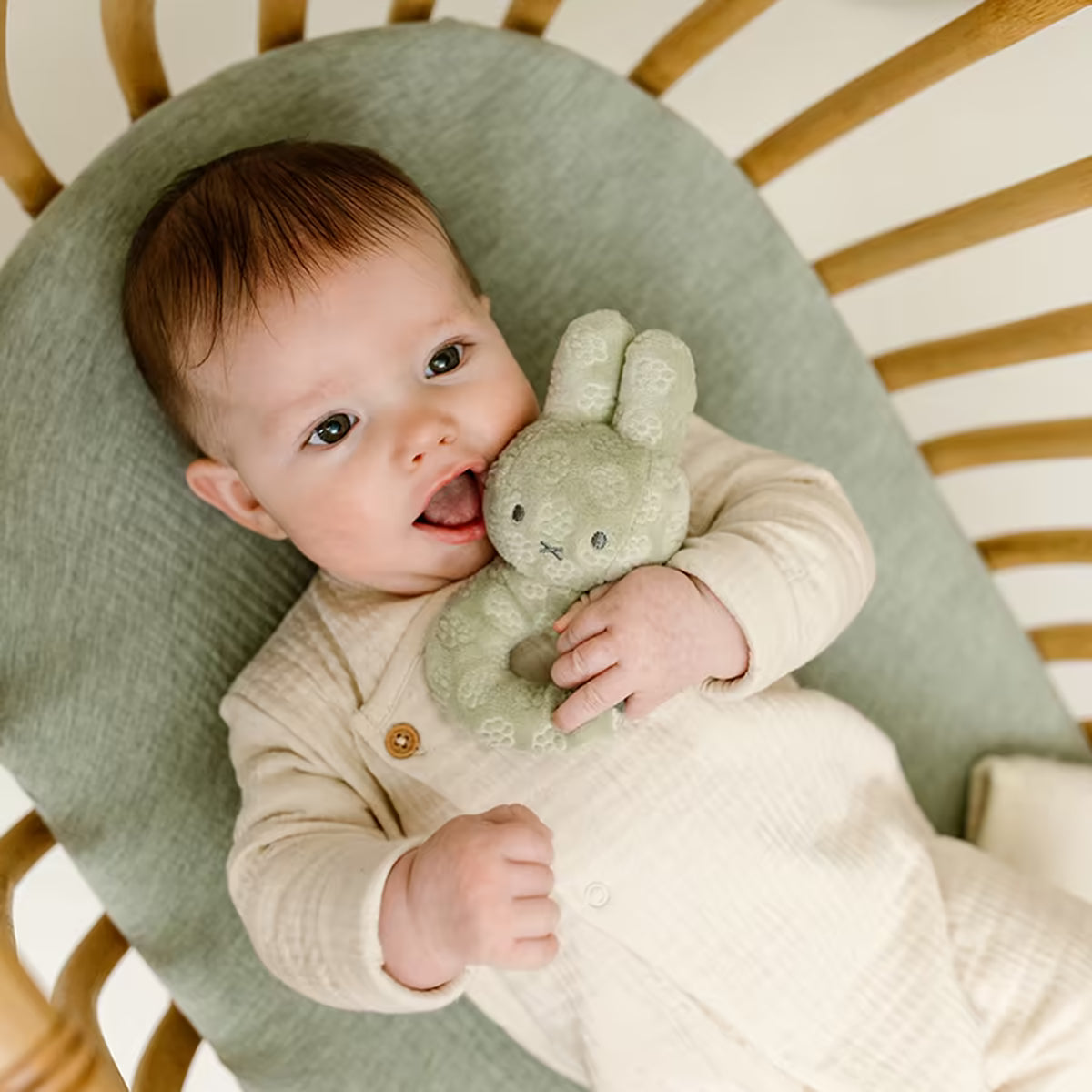 Baby ligt in wieg en knuffelt met Nijntje Rammelaar Green Flower, ideaal baby cadeau en educatief speelgoed.