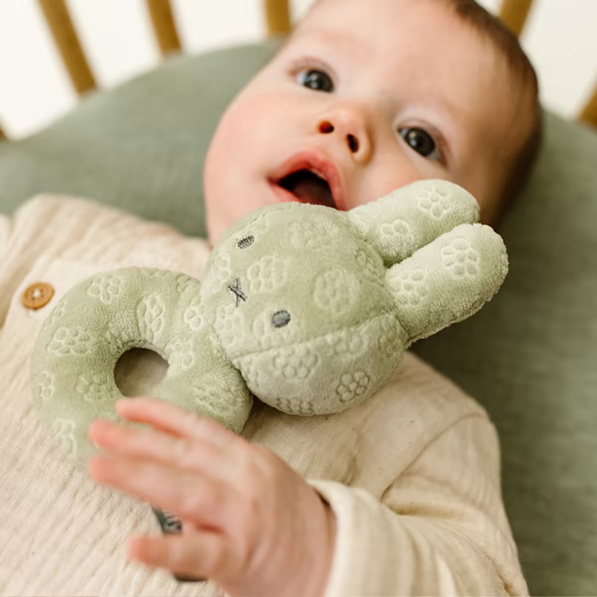 Baby in ledikant speelt met zachte Nijntje Rammelaar Green Flower, ideaal baby speelgoed en sensorisch speelgoed.