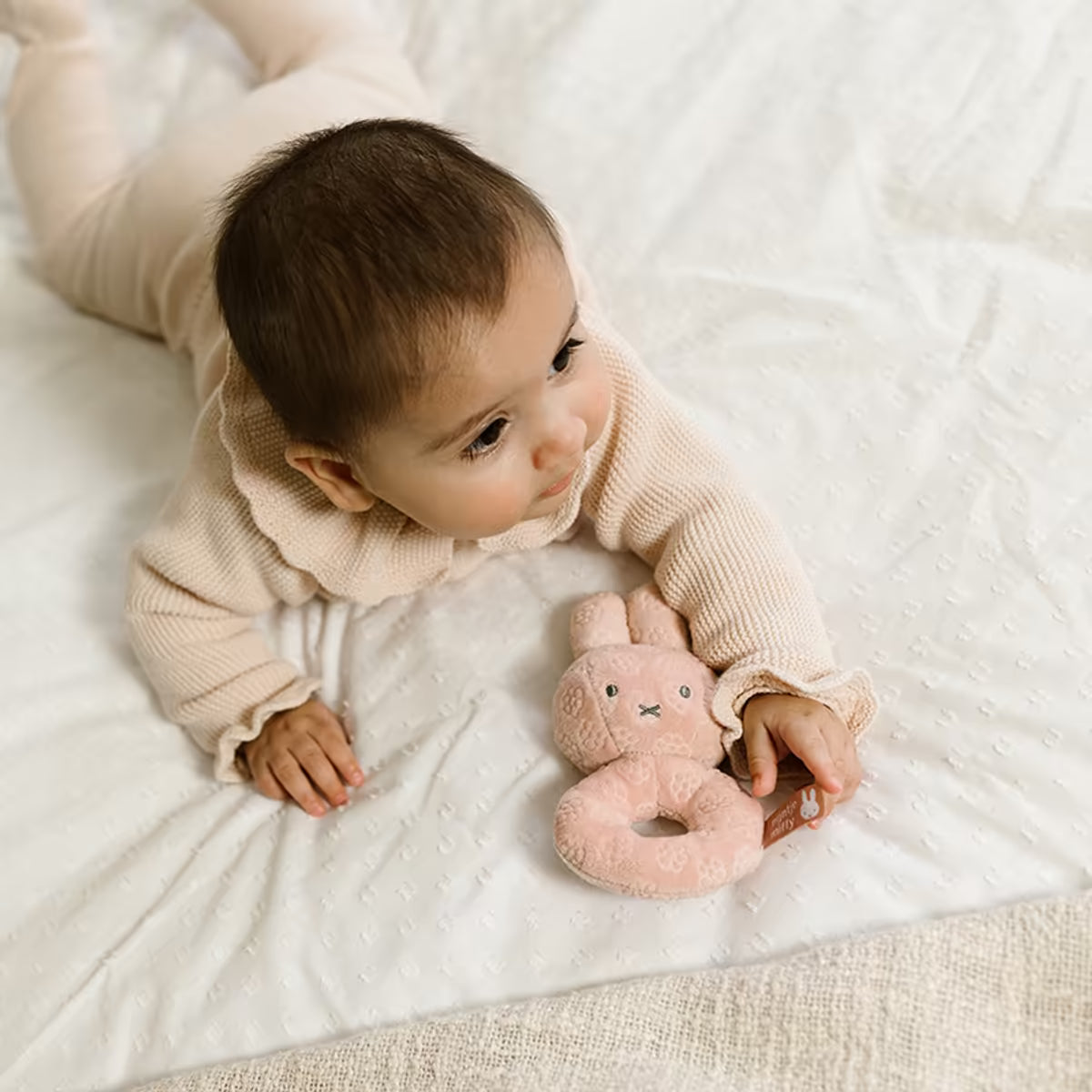 Baby op bed met roze Nijntje Rammelaar Pink Flower, lief kraamcadeau en veilig baby speelgoed voor eerste maanden.
