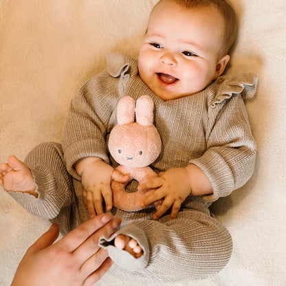 Blije baby met Nijntje Rammelaar Pink Flower in grijs boxpakje, ideaal baby speelgoed en zacht kraamcadeau.