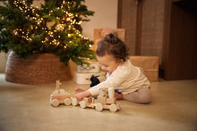Peuter speelt onder kerstboom met houten speelgoed trein van Jollein, perfect als baby cadeau of decoratie.