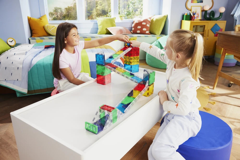 Kinderen bouwen samen een Rail Racers Deluxe knikkerbaan magnetisch in een vrolijke meisjeskamer.