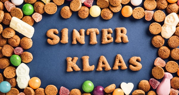 Feestelijk foto met Sinterklaasletters van koek en kleurrijke pepernoten op blauwe achtergrond.