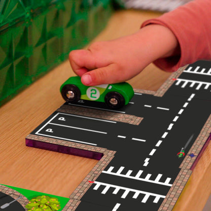 Close-up kinderhand duwt groene Coblo auto over magneet wegtegel met parkeerplaats