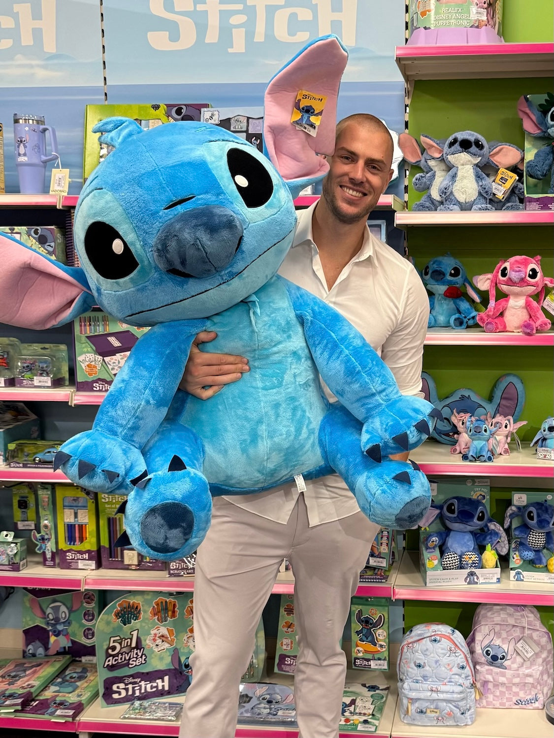 eigenaar en co founder William staat in een speelgoed winkel met Stitch knuffel kijkt blij.