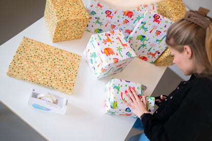 Vrouw inpakt kraamcadeau met kleurrijk jungleprint papier en goudstipjes, Sproutz cadeauverpakking