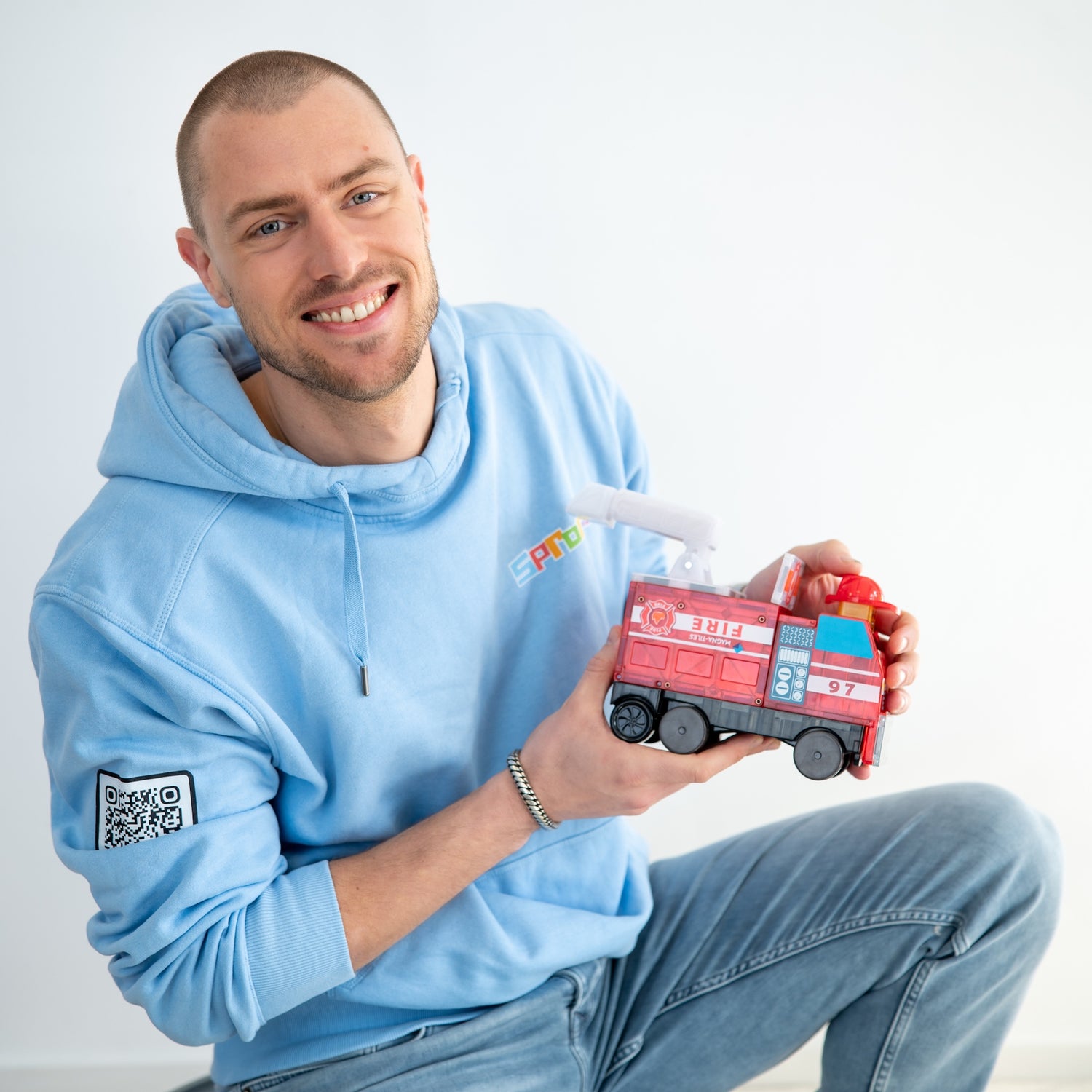 Eigenaar William portret met rode brandweerauto magnetisch speelgoed, blauwe Sproutz hoodie zichtbaar