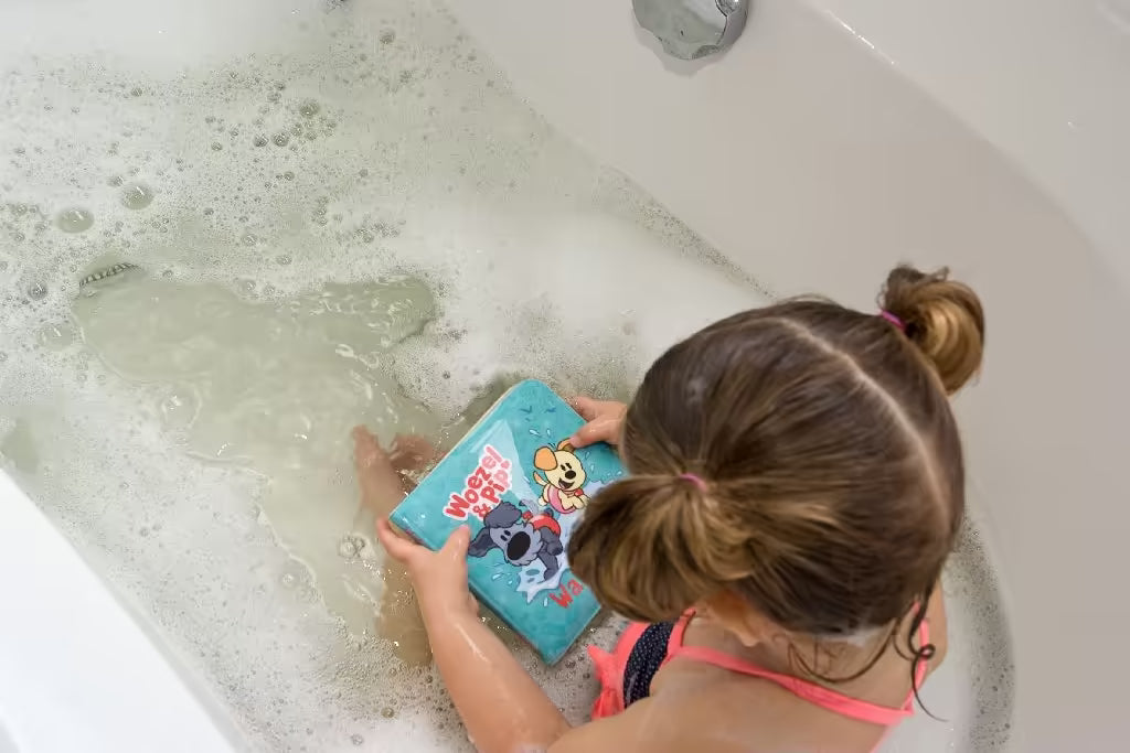 Peuter leest Woezel en Pip badboekje in schuimend bad, kleurrijk badspeelgoed en vrolijk leesplezier in bad
